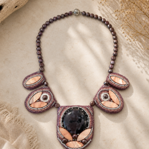 Statement necklace featuring plum pearl beads, blush shell accents, and intricate bead embroidery surrounding a dramatic floral-patterned cabochon centerpiece.