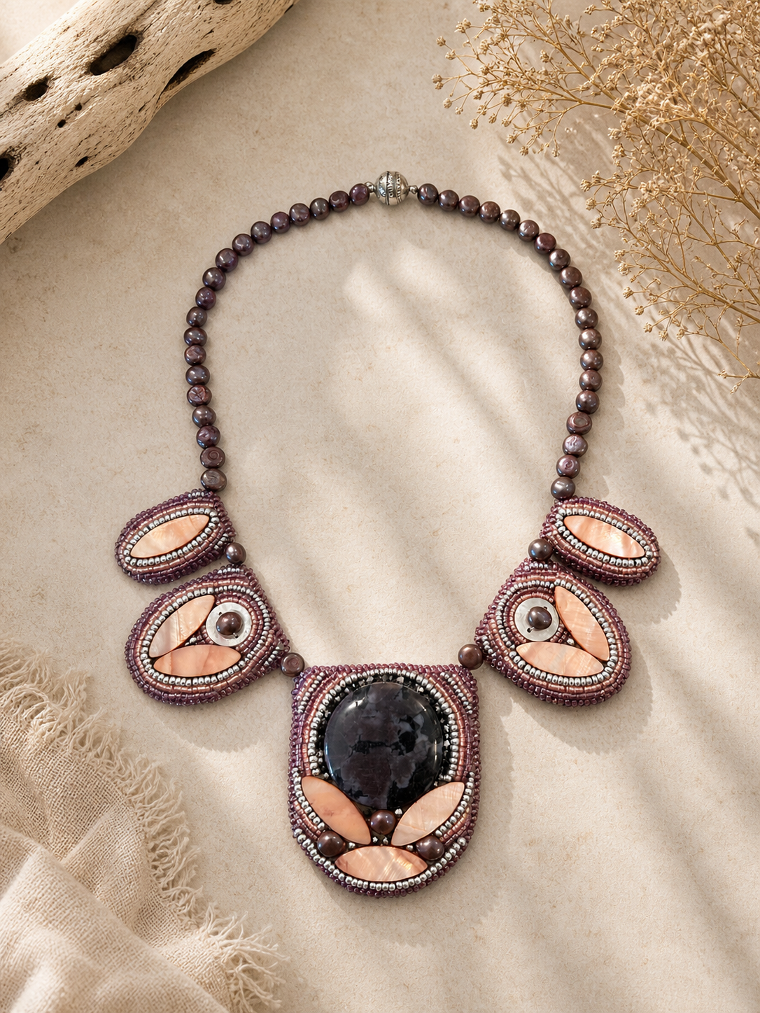 Statement necklace featuring plum pearl beads, blush shell accents, and intricate bead embroidery surrounding a dramatic floral-patterned cabochon centerpiece.