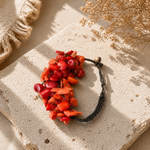 Bold statement bracelet featuring clustered coral-red and orange chip beads woven onto dark braided cords with an organic, sculptural silhouette.