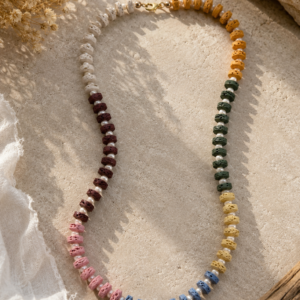 Pastel lava stone necklace with pearl spacer beads in cream, mustard, green, burgundy, pink, and blue tones with gold clasp.