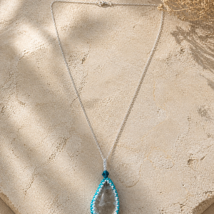 Minimalist pendant necklace featuring a clear teardrop-shaped stone framed in turquoise and silver bead embroidery, suspended from a delicate silver chain with a faceted blue crystal accent.