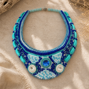 Statement necklace featuring layered turquoise, cobalt, and icy blue bead embroidery with crystal accents, crescent turquoise stones, and a bold sapphire-toned center stone.