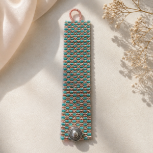 Wide loom-woven bracelet in turquoise and dusty rose seed beads with a geometric checkerboard pattern and silver-tone button clasp.