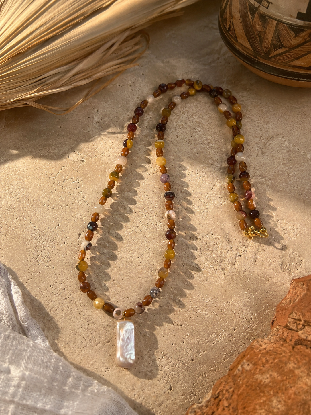 Mookite jasper bead necklace in warm earth tones with a rectangular freshwater pearl pendant and gold clasp.