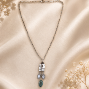 Delicate silver-toned pendant necklace featuring hammered metal, floral glass accents, and a moss-green drop displayed on soft ivory fabric.