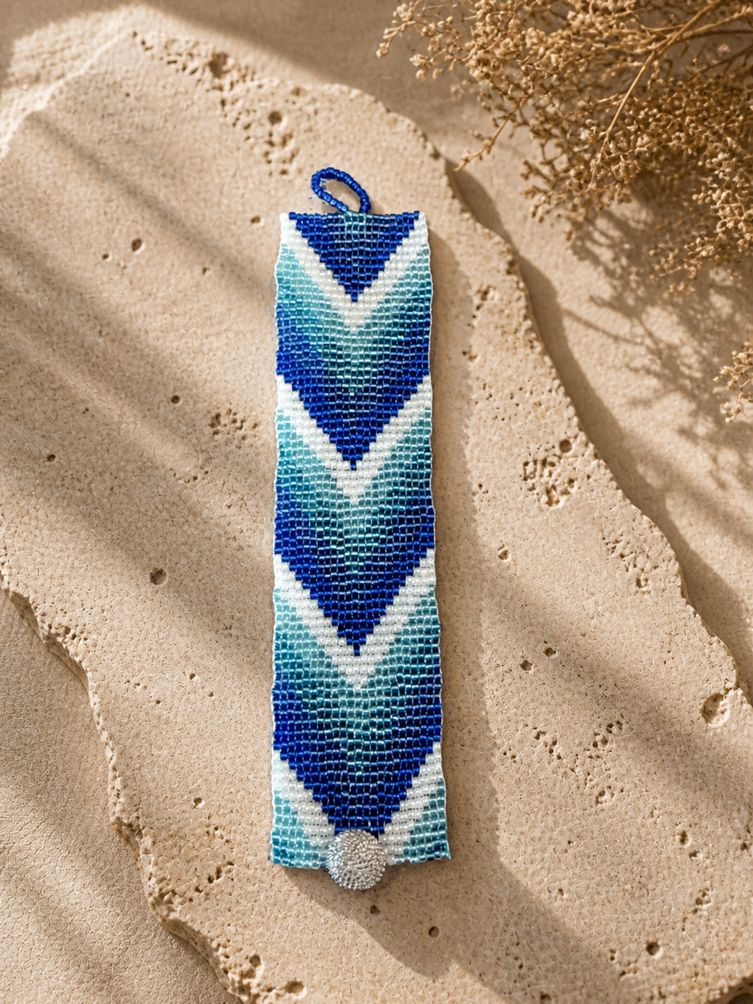 Loom-woven bracelet in layered blue, aqua, and white chevron pattern with silver button clasp.