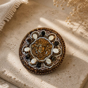 Circular bead embroidered brooch with bronze Medusa centerpiece, pearl accents, and black crystal details.