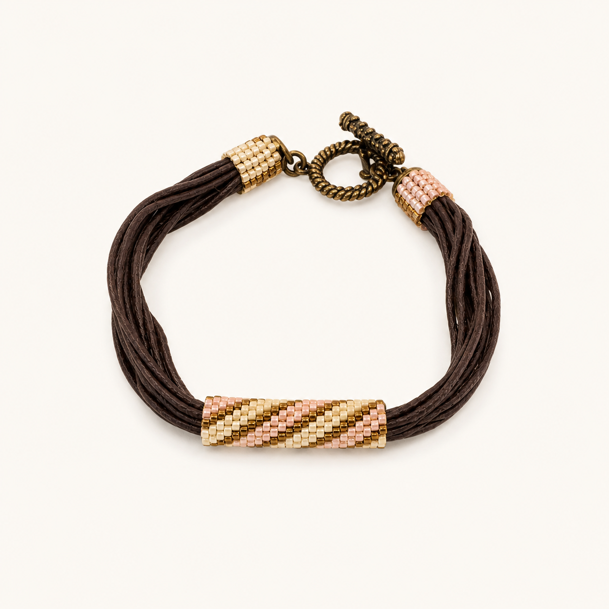 Multi-strand brown cord bracelet with soft pink and gold beadwoven accents and bronze toggle clasp.