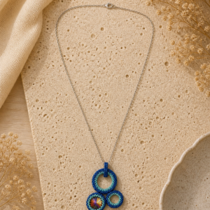 Blue circular beaded pendant necklace with layered geometric forms and an iridescent crystal focal on a silver-tone chain.