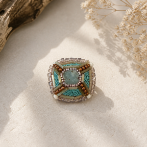 Square geometric bead-embroidered brooch in aqua, bronze, cream, and smoky neutral tones with layered architectural beadwork.