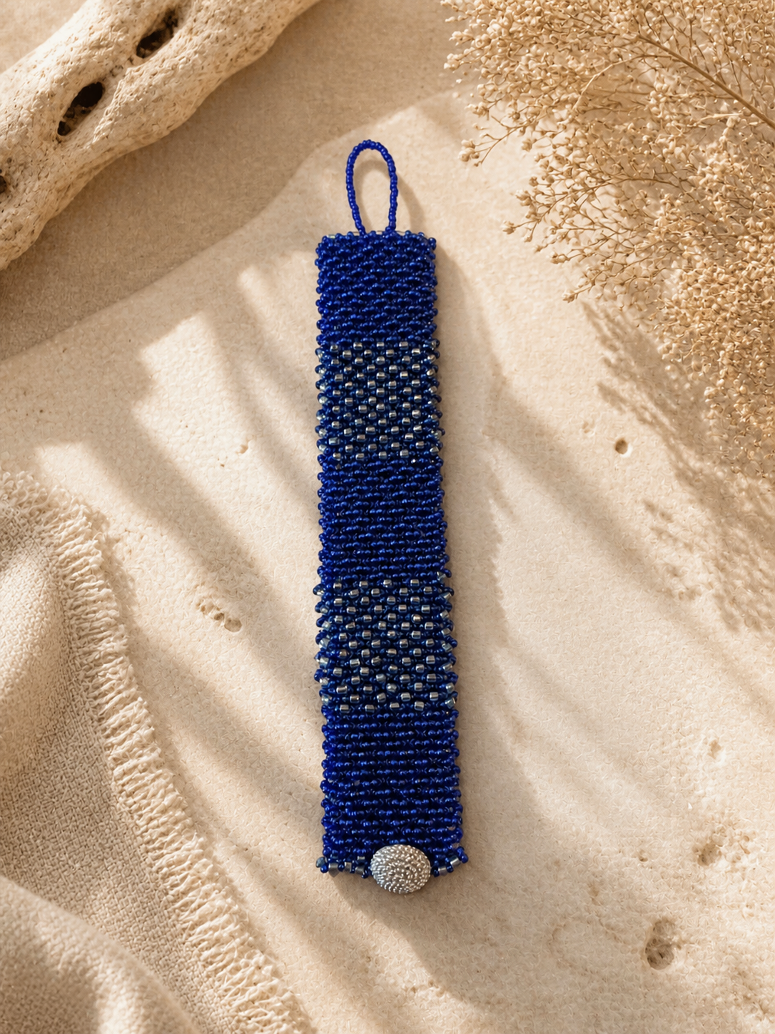 Handwoven cobalt blue bead bracelet with metallic accent bands and textured button closure.