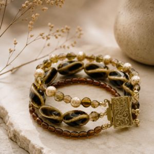 Multi-strand bracelet featuring warm amber and brown artisan glass beads, freshwater pearls, crystal accents, and an ornate gold-toned clasp.