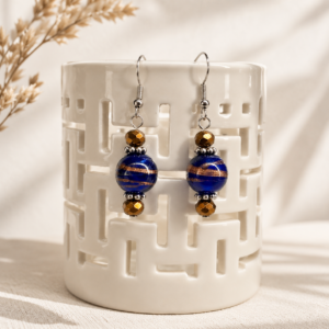 Handmade earrings featuring cobalt blue lampwork glass beads with copper-gold swirls, accented by bronze crystal beads and sterling silver ear wires, displayed on a cream ceramic stand.