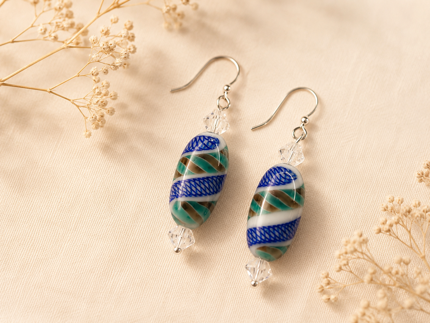 Handcrafted drop earrings with oval lampwork glass beads featuring cobalt blue, seafoam green, white, and tan swirls, accented by clear faceted crystals and sterling silver ear wires.