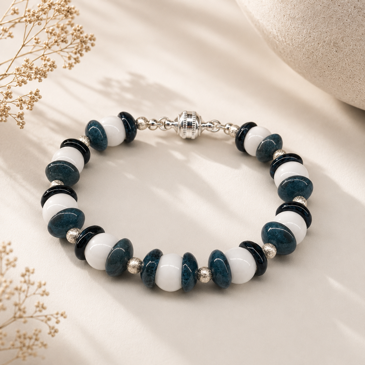Handcrafted bracelet featuring navy blue lampwork glass disc beads, white glass beads, sterling silver accents, and a silver magnetic clasp arranged in an alternating contemporary pattern.