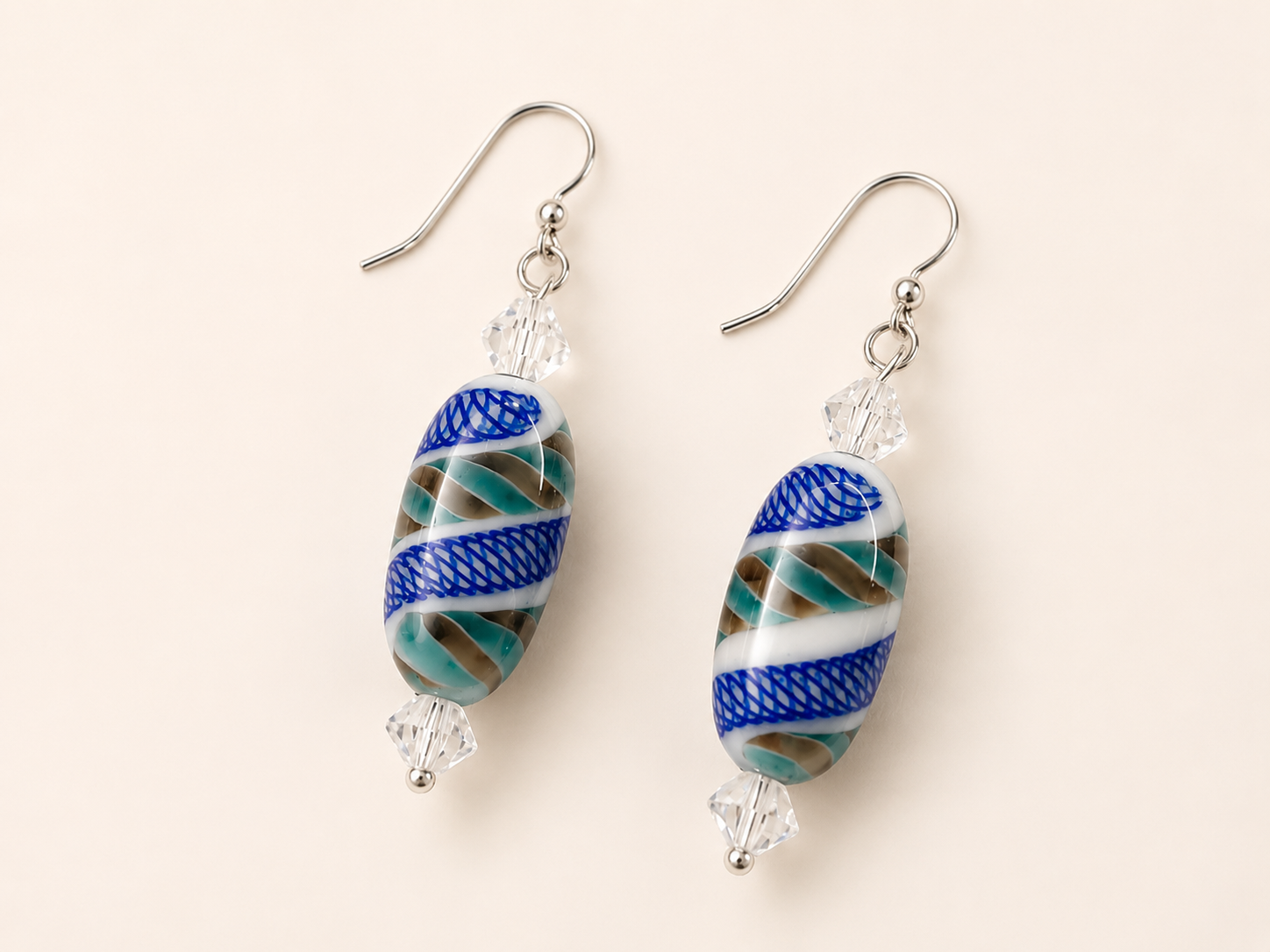 Handcrafted drop earrings with oval lampwork glass beads featuring cobalt blue, seafoam green, white, and tan swirls, accented by clear faceted crystals and sterling silver ear wires.