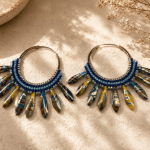 Large handcrafted hoop earrings featuring layered blue beadwork and artisan glass dagger beads in shades of cobalt blue, gold, cream, and brown arranged in a dramatic fan design.