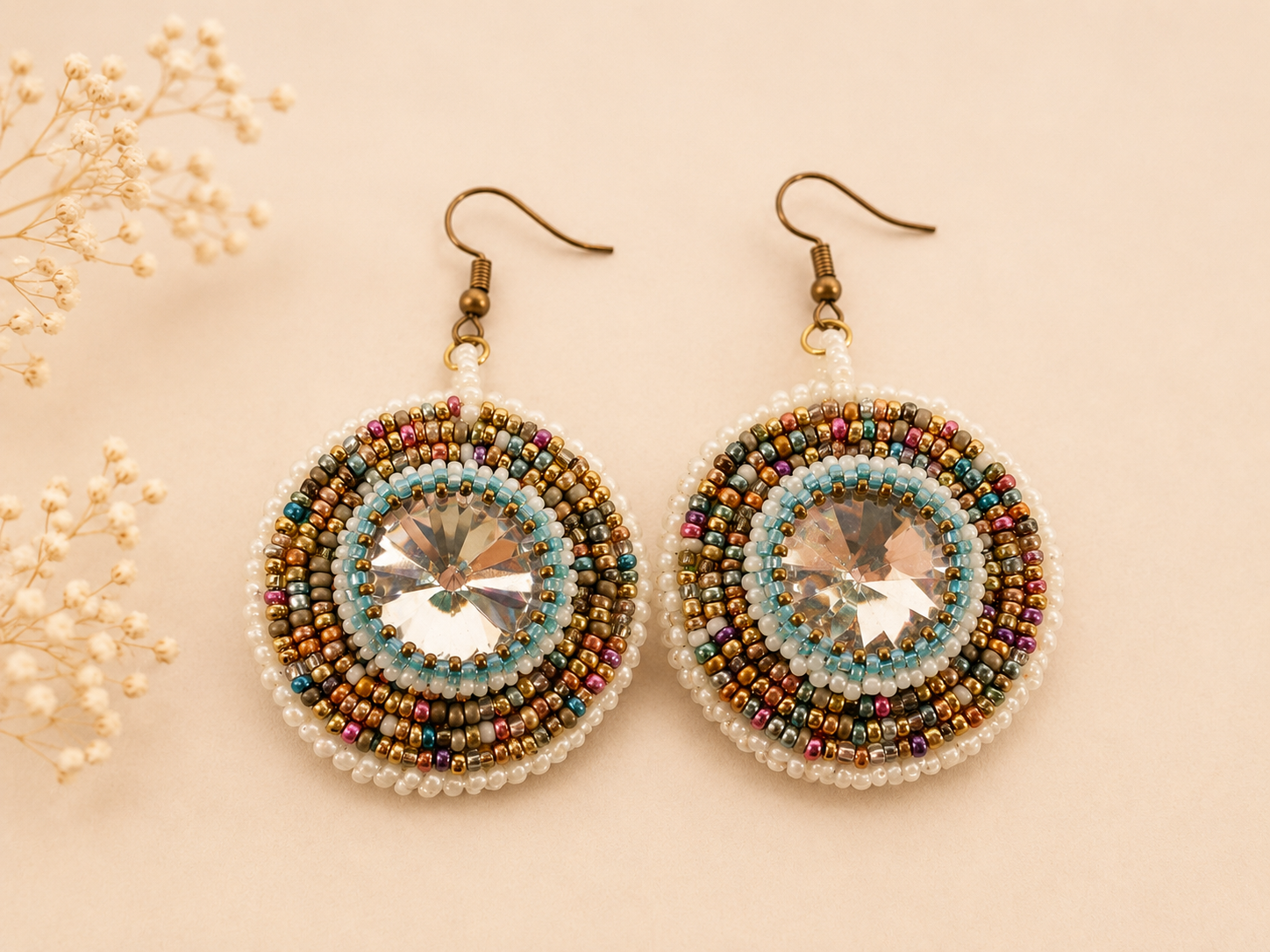 Handcrafted bead embroidered earrings featuring large crystal rivolis surrounded by concentric rings of white, aqua, gold, bronze, teal, and berry seed beads.