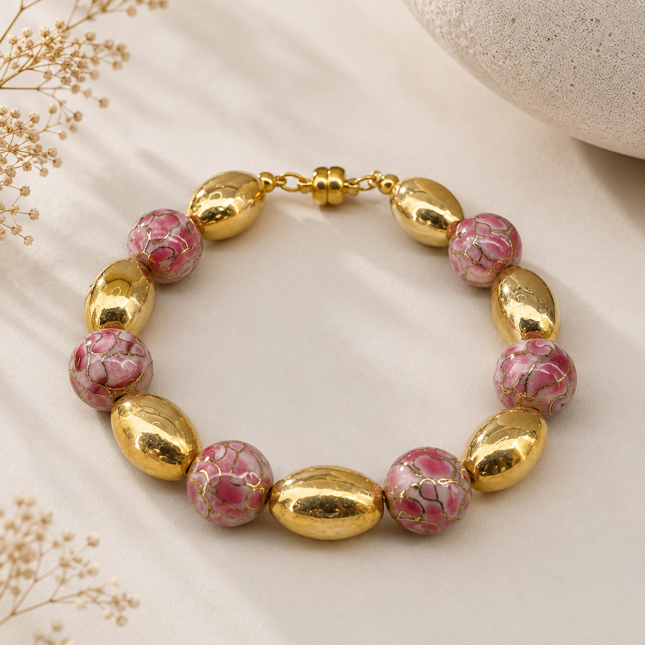 Handcrafted bracelet featuring pink artisan beads with gold veining, large gold-toned oval beads, and a gold-toned magnetic clasp arranged in an alternating pattern.