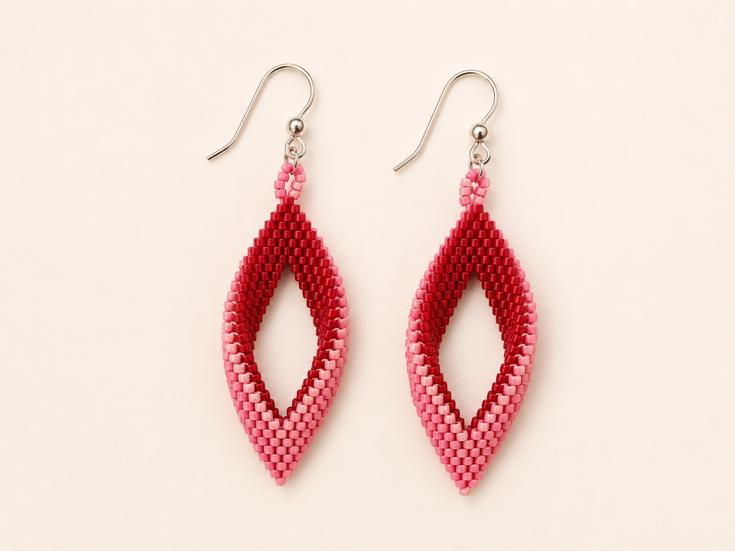 Handwoven geometric earrings featuring a twisted open diamond shape created from red and pink Miyuki seed beads with sterling silver ear wires.