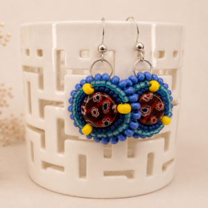 Handcrafted bead embroidered earrings featuring patterned artisan glass cabochons surrounded by cobalt blue, turquoise, navy, and yellow seed bead embroidery.