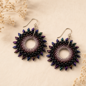 Handwoven circular earrings featuring black, plum, and lavender beadwork with iridescent purple and blue dagger beads forming a radiant halo around an open center.