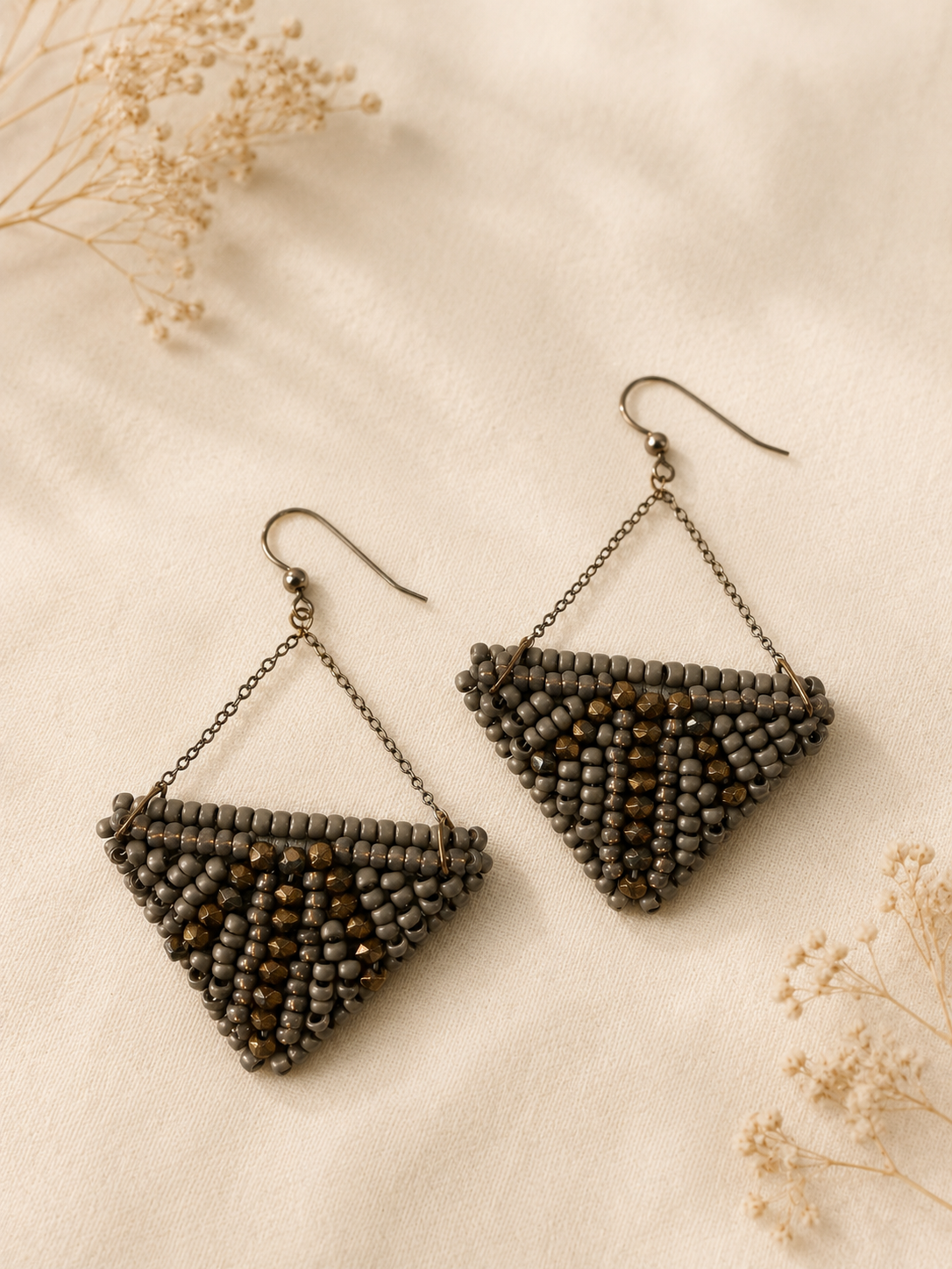 Handwoven triangular earrings featuring graphite gray seed beads, bronze metallic accents, and suspended chain details forming a modern geometric silhouette.