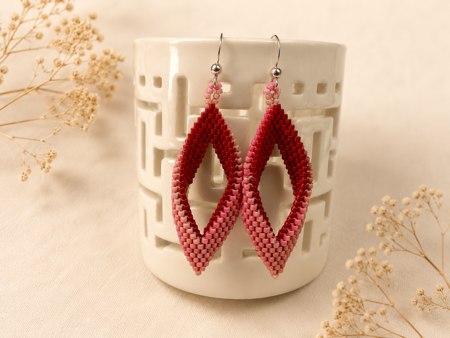 Handwoven geometric earrings featuring a twisted open diamond shape created from red and pink Miyuki seed beads with sterling silver ear wires.
