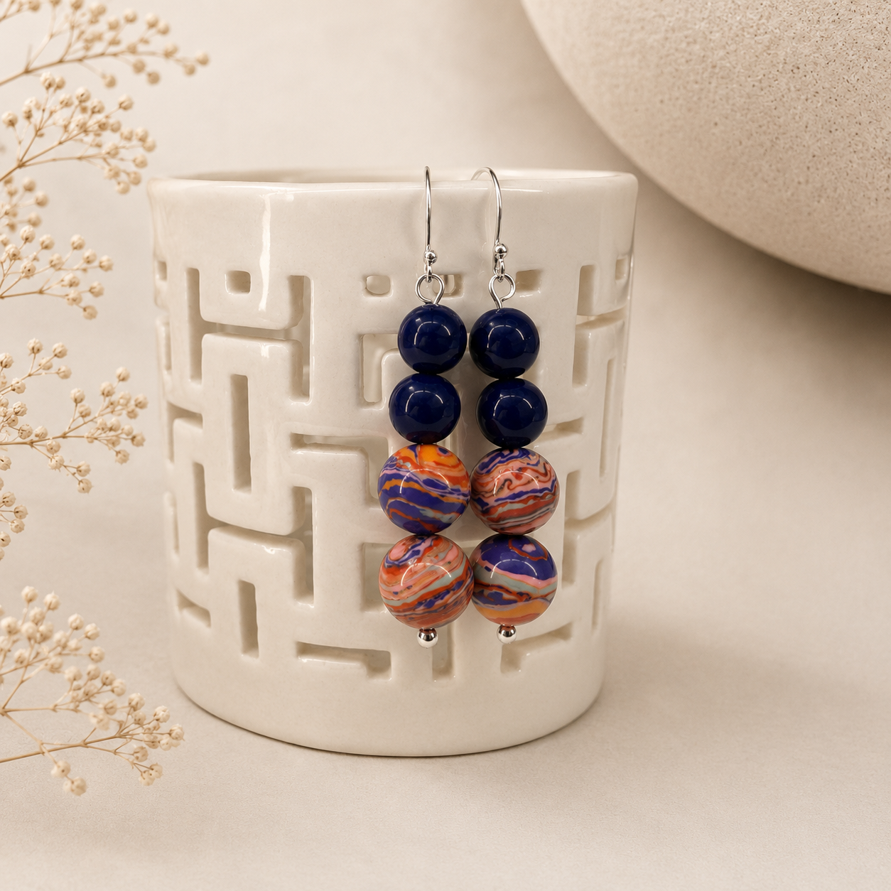 Handcrafted drop earrings featuring cobalt blue glass beads and artisan focal beads swirled with coral, peach, violet, and blue tones on sterling silver ear wires.