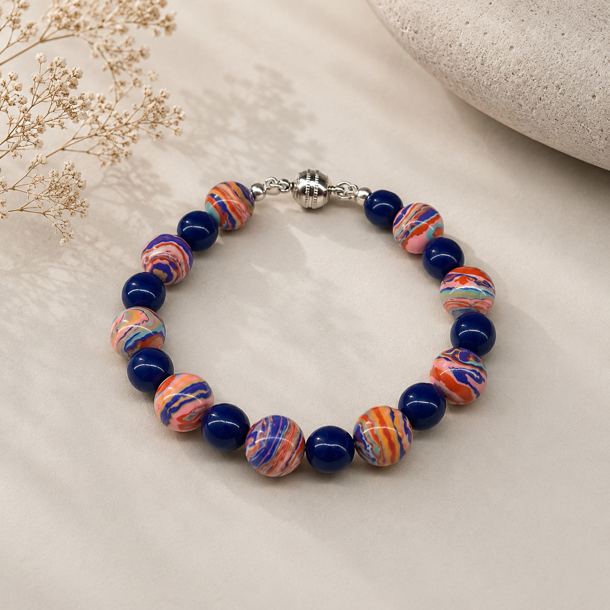 Handcrafted bracelet featuring multicolored artisan beads with swirling coral, blue, lavender, turquoise, and peach patterns, accented with cobalt blue glass beads and a silver magnetic clasp.