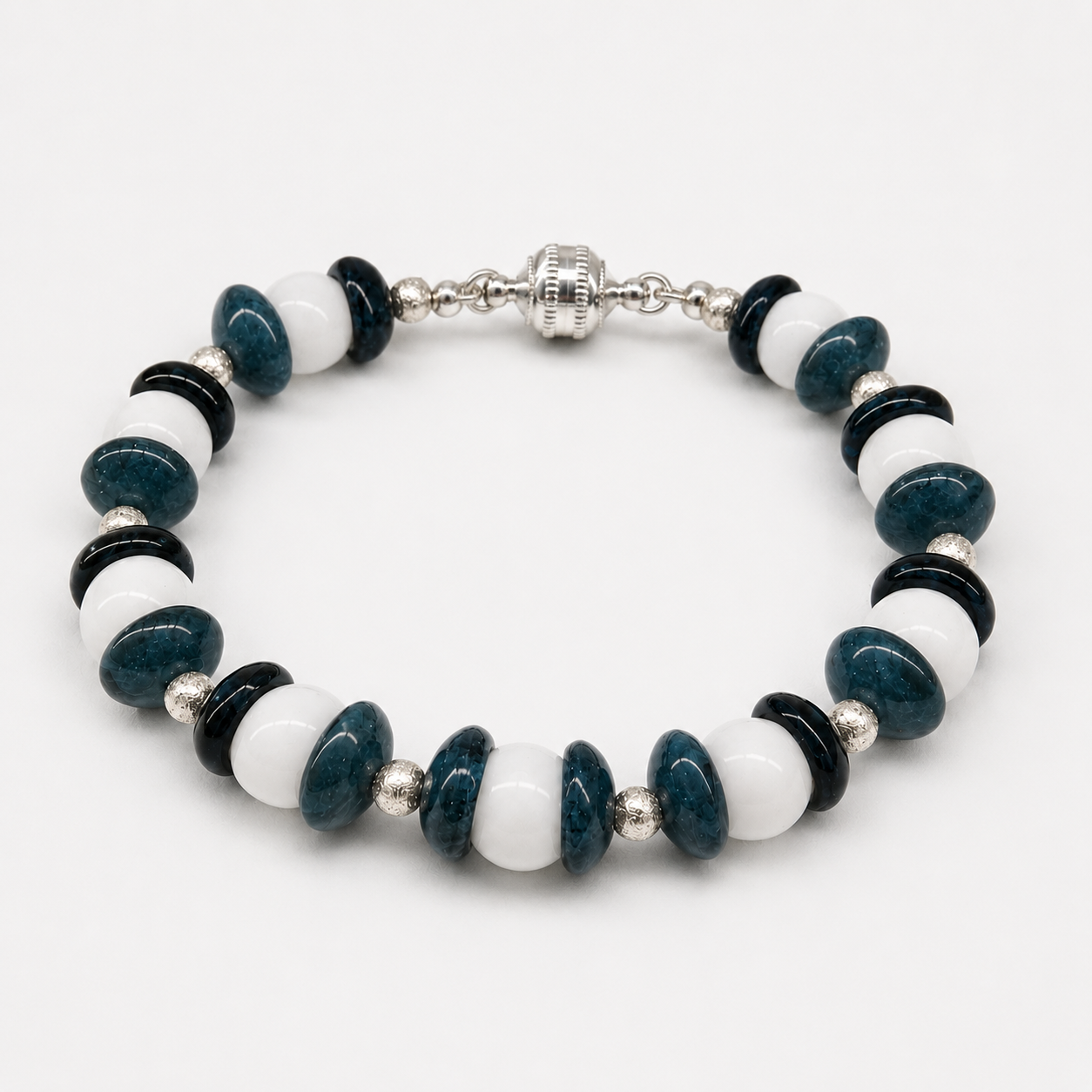 Handcrafted bracelet featuring navy blue lampwork glass disc beads, white glass beads, sterling silver accents, and a silver magnetic clasp arranged in an alternating contemporary pattern.